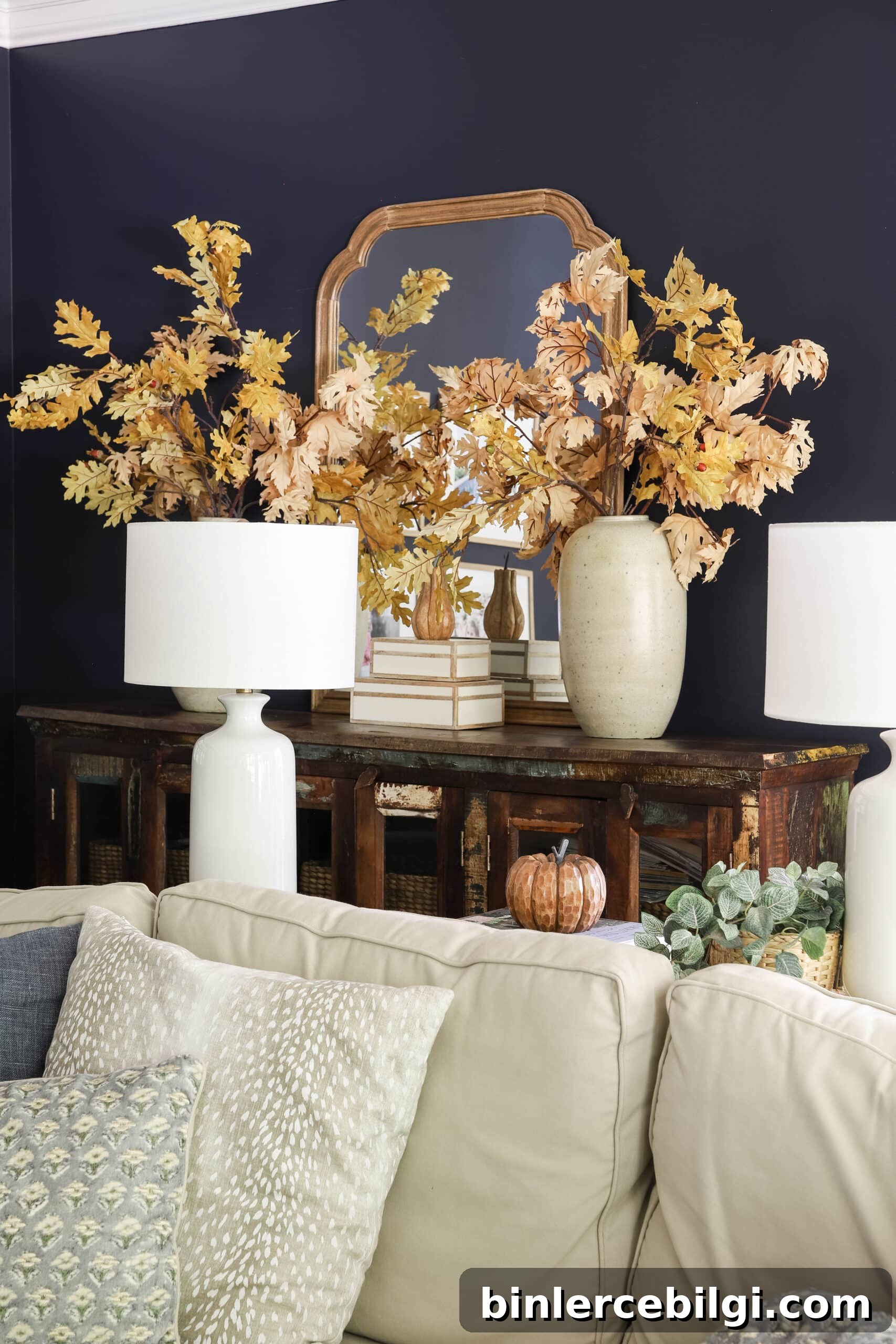 Leafy autumn oak stems in earthen vases in a living room with navy walls.