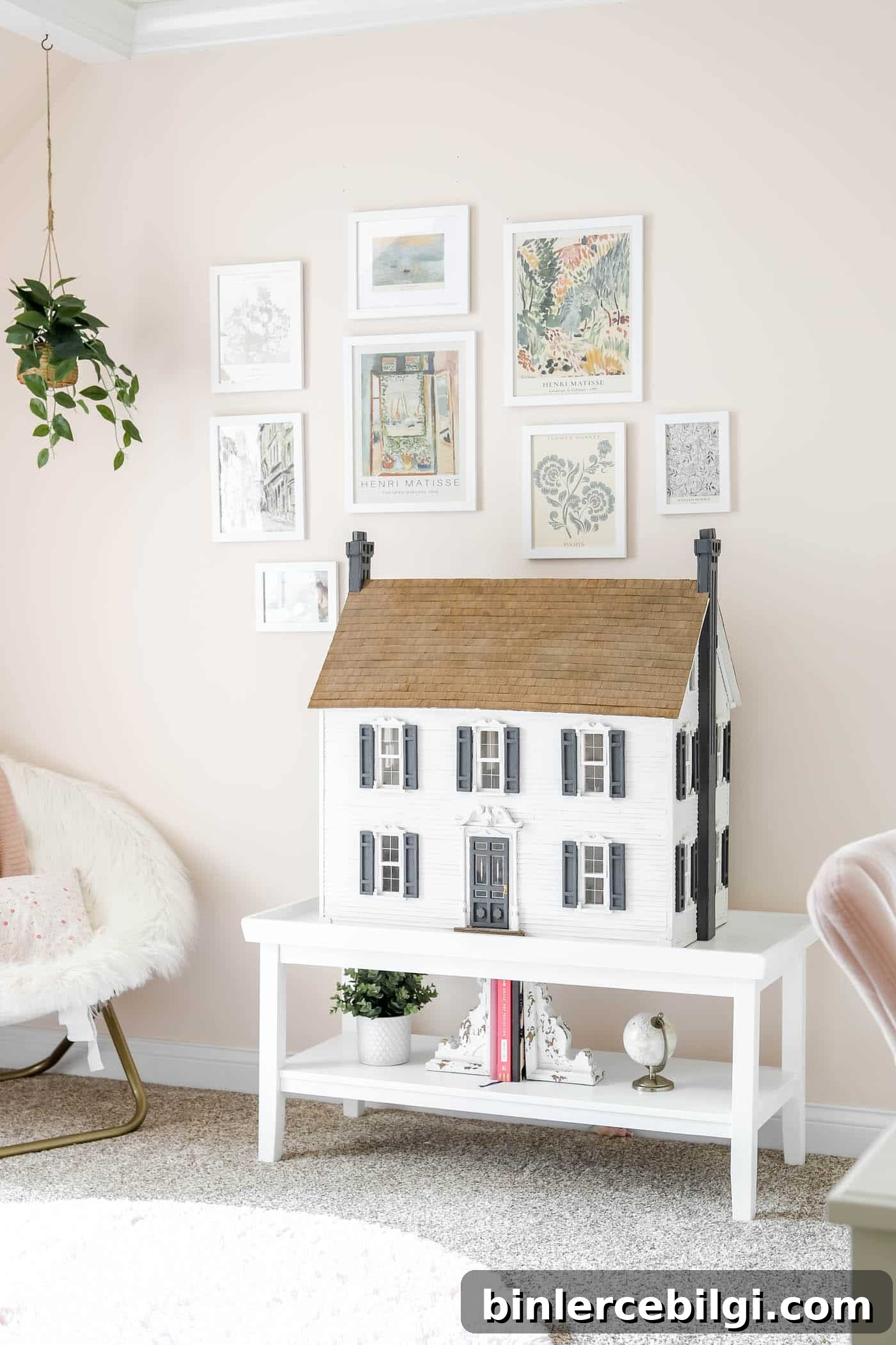 gallery wall on a pink wall with a dollhouse on a coffee table.