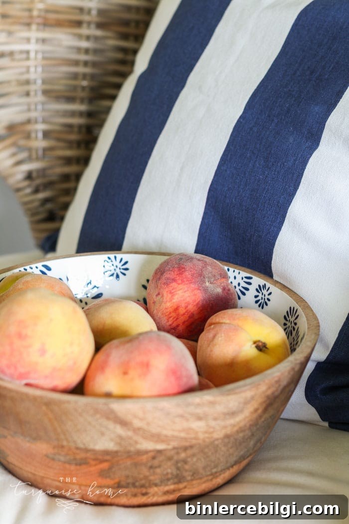 Summer Tablescape Ideas for Al Fresco Entertaining 12 peaches in a bowl with a striped navy and white pillow.