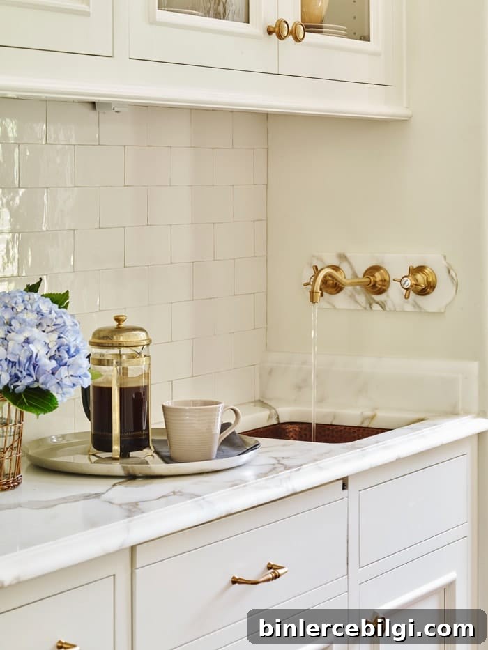 white butler's pantry with subway tile backsplash, marble countertop, brass faucet and small copper sink.