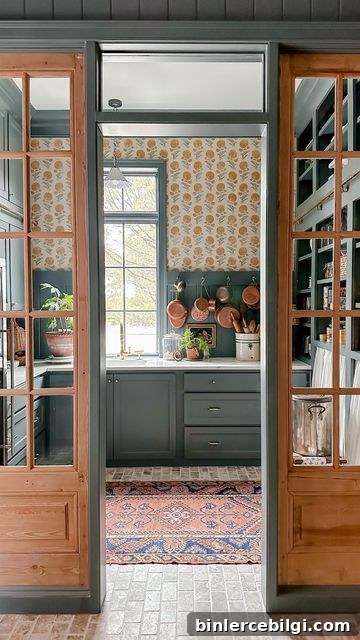 Funky scullery with brick flooring, green painted cabinets and bold wallpaper.