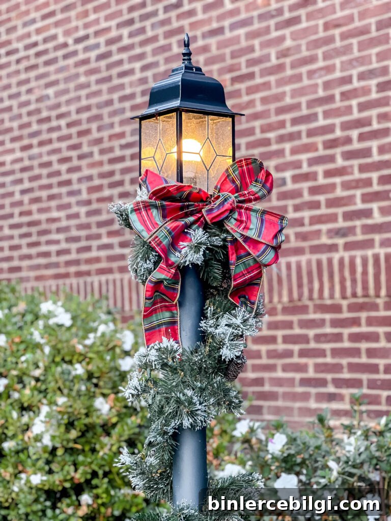 Lamppost with christmas garland and red plaid ribbon on it.