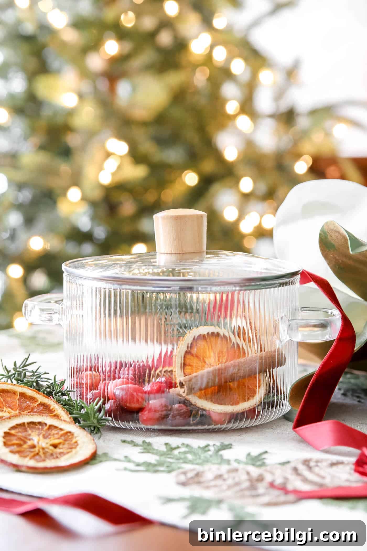 DIY Christmas Simmer Pot Recipe with Free Printable Gift Tags 7 rosemary, oranges and cinnamon in a clear pot in front of a Christmas tree.