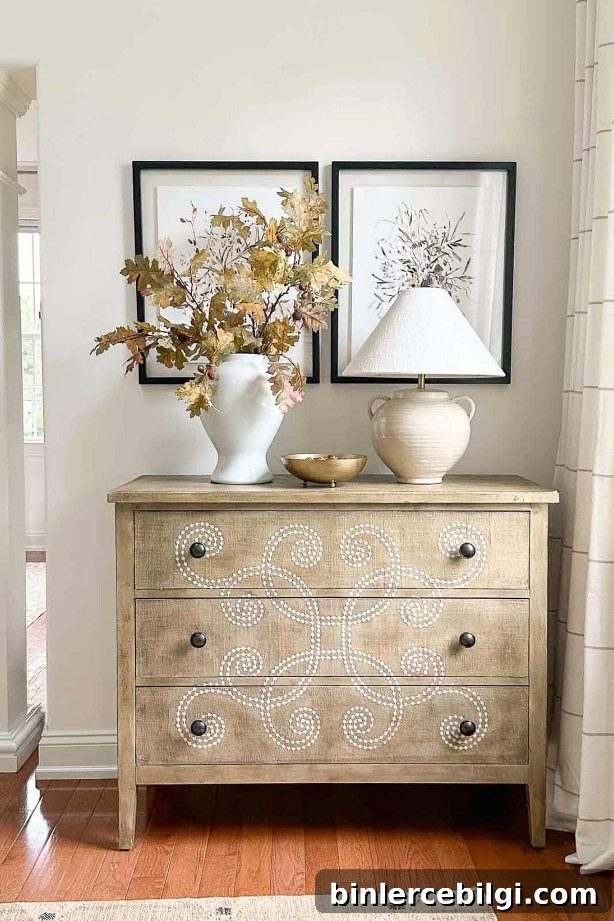 light wood dresser with fall foliage in a vase and a lamp.