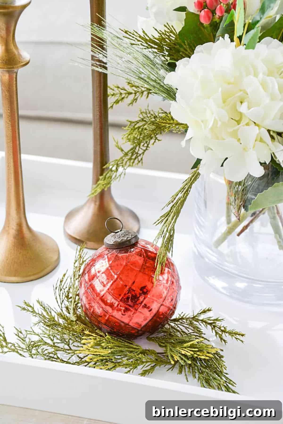 red ornament on some greenery next to flowers and candlesticks.