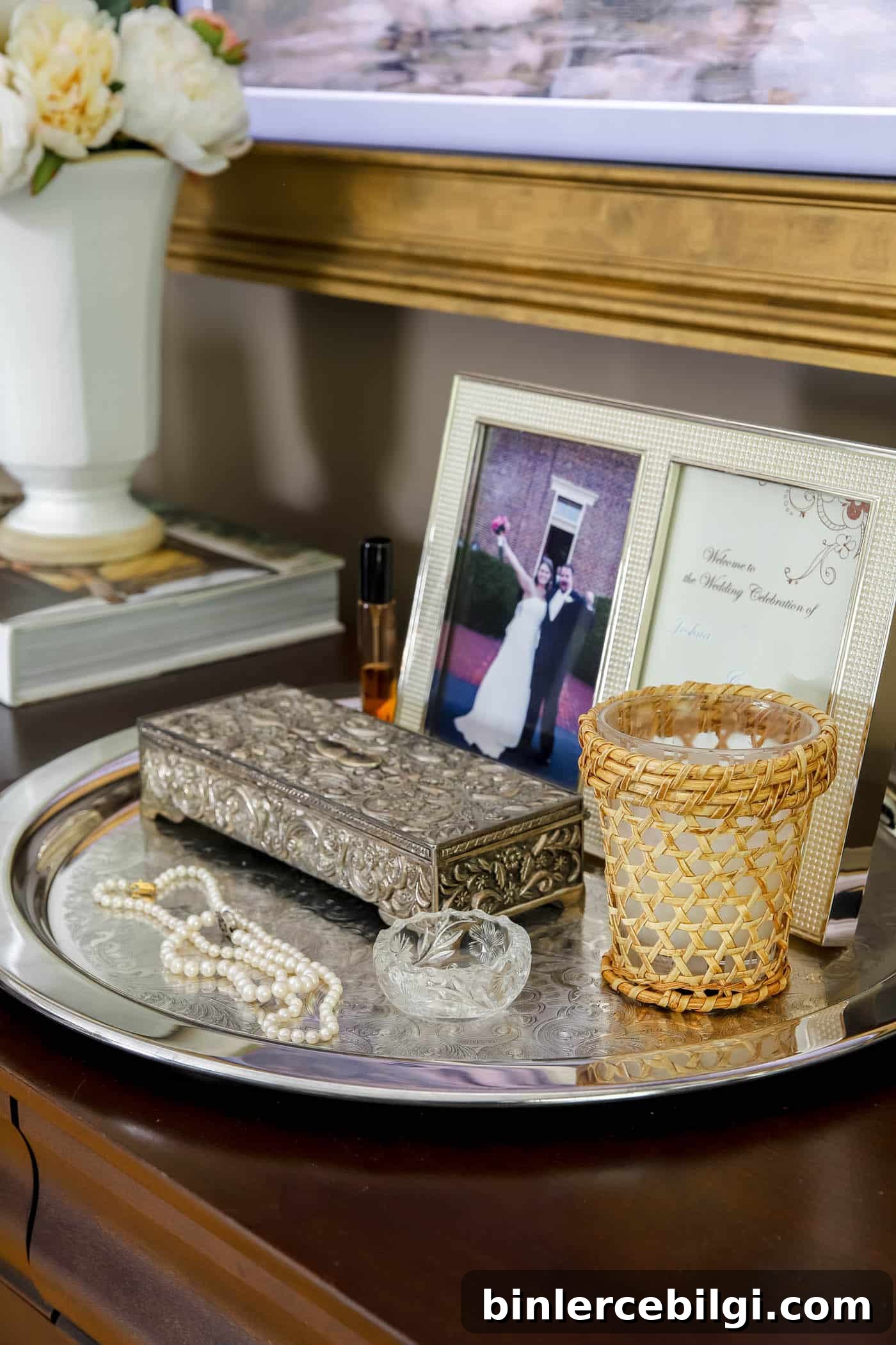 silver tray on a bedroom dresser holding a framed photo, jewelry box and pearl necklaces.